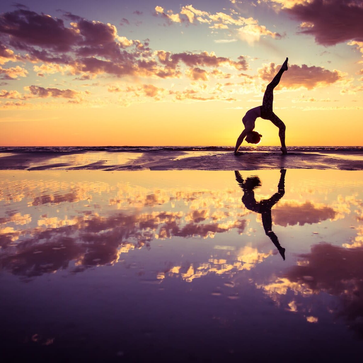 silhouette of woman practicing yoga on the beach at sunset